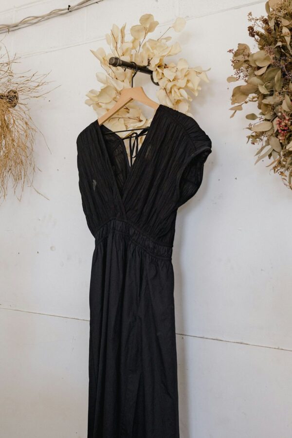 Black crossover dress on a wooden hanger against a white wall hung with dried wreaths.