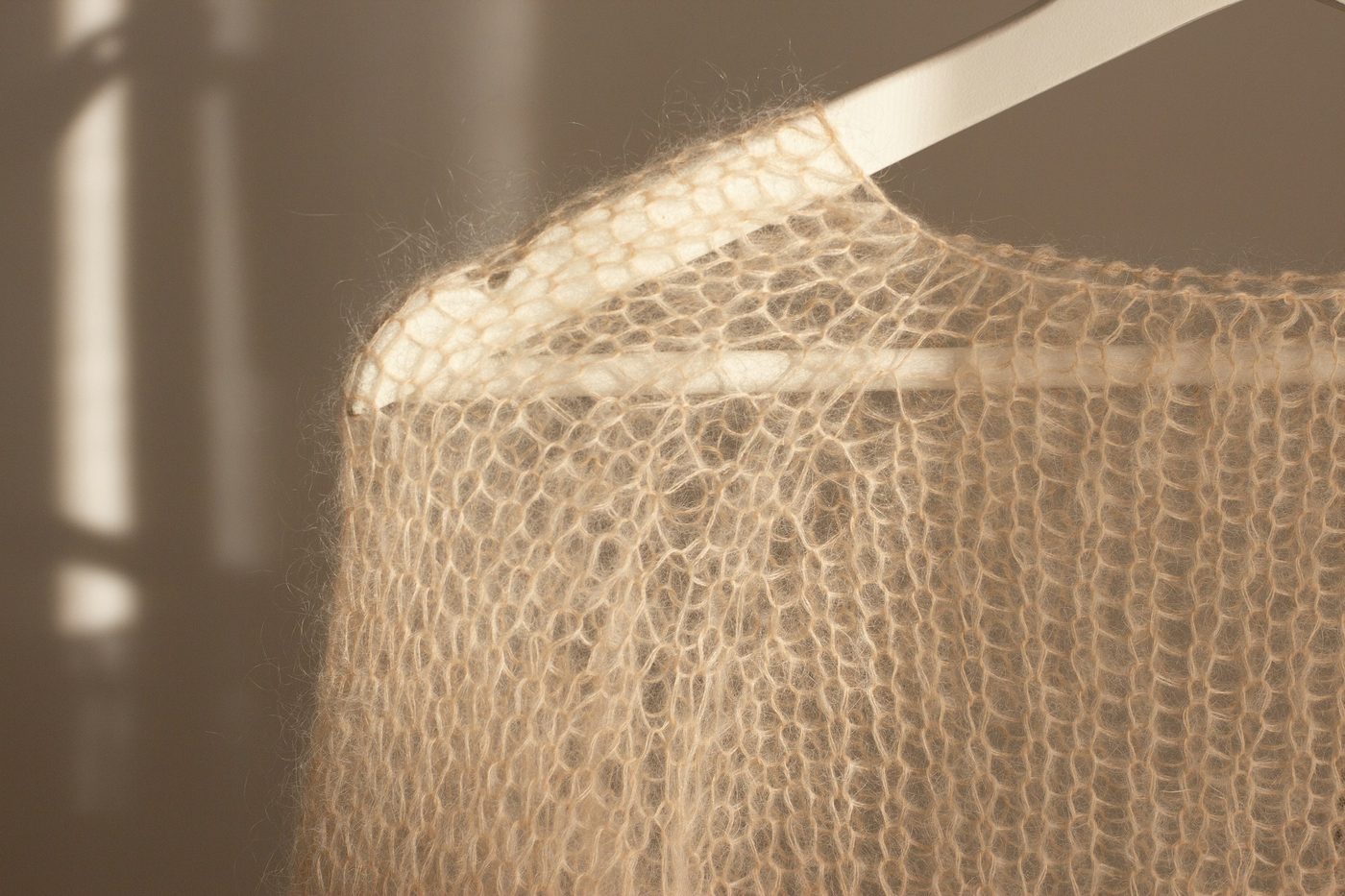 A sheer mohair knit on a white hanger in afternoon light.
