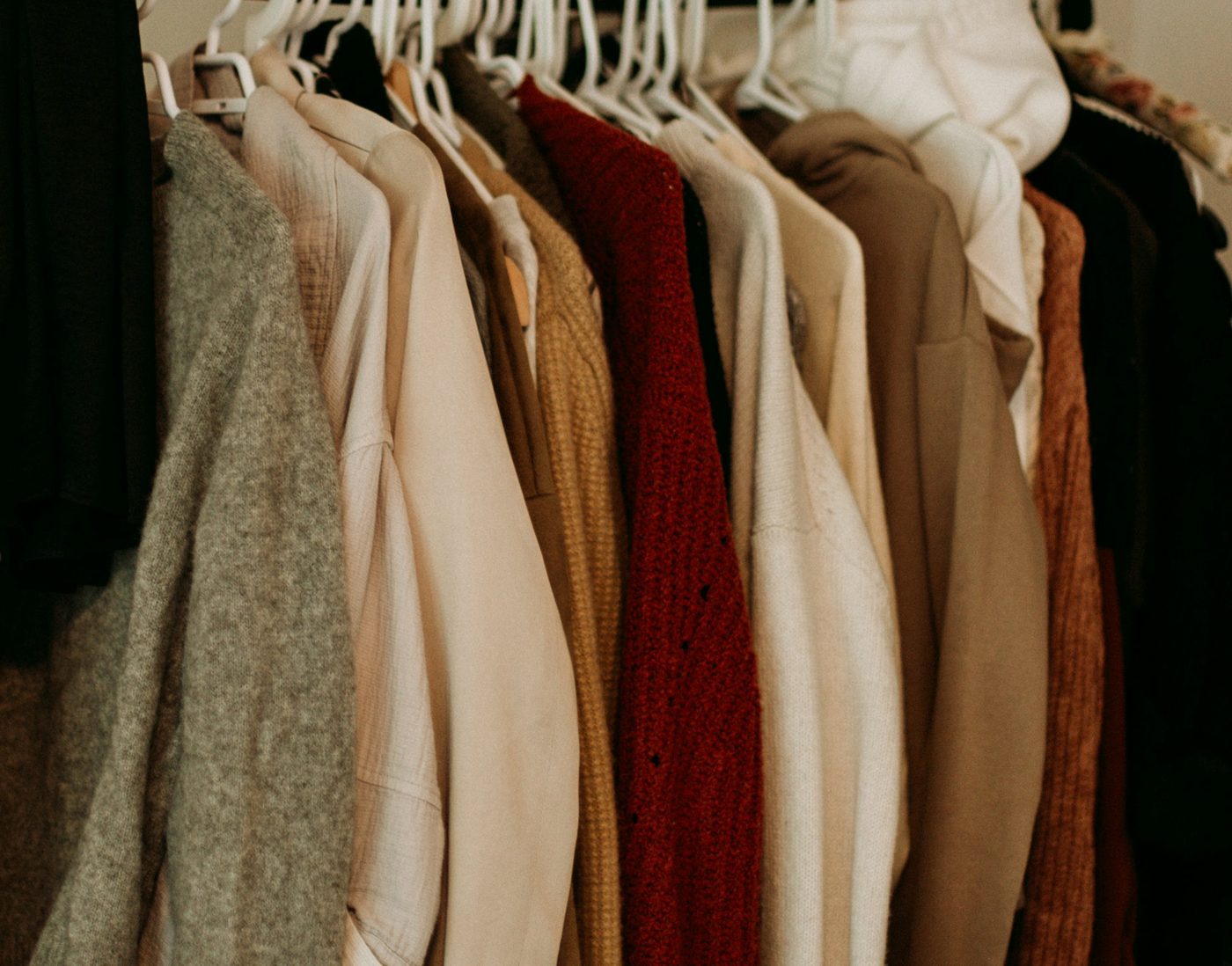 Knitwear, shirts and jackets in cream, grey, mustard and red on white hangers.