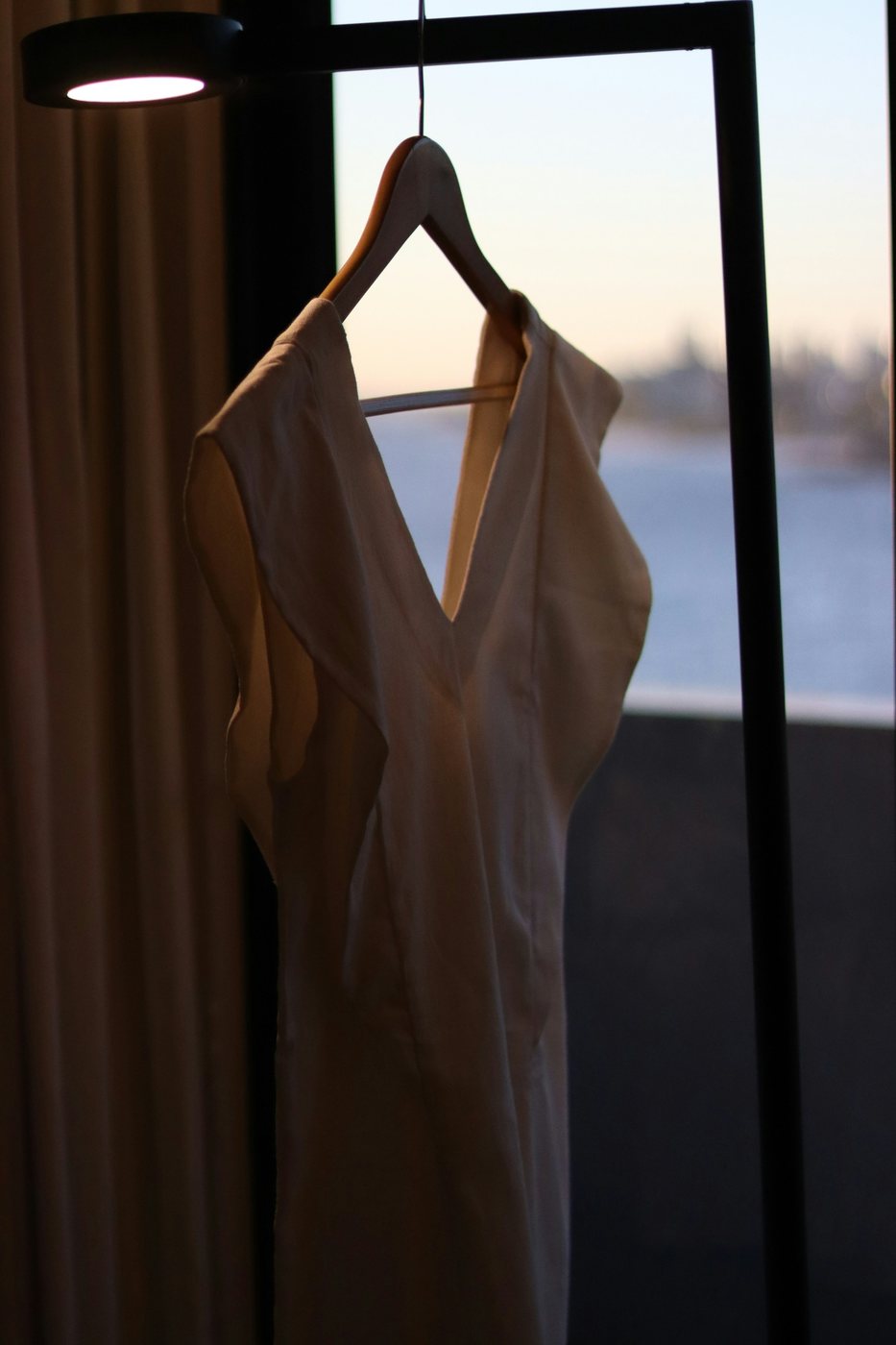 Cream V-neck dress on a hanger by a window at dusk.