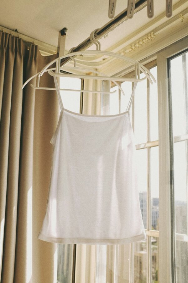 White cami top on a hanger by a sunlit window.