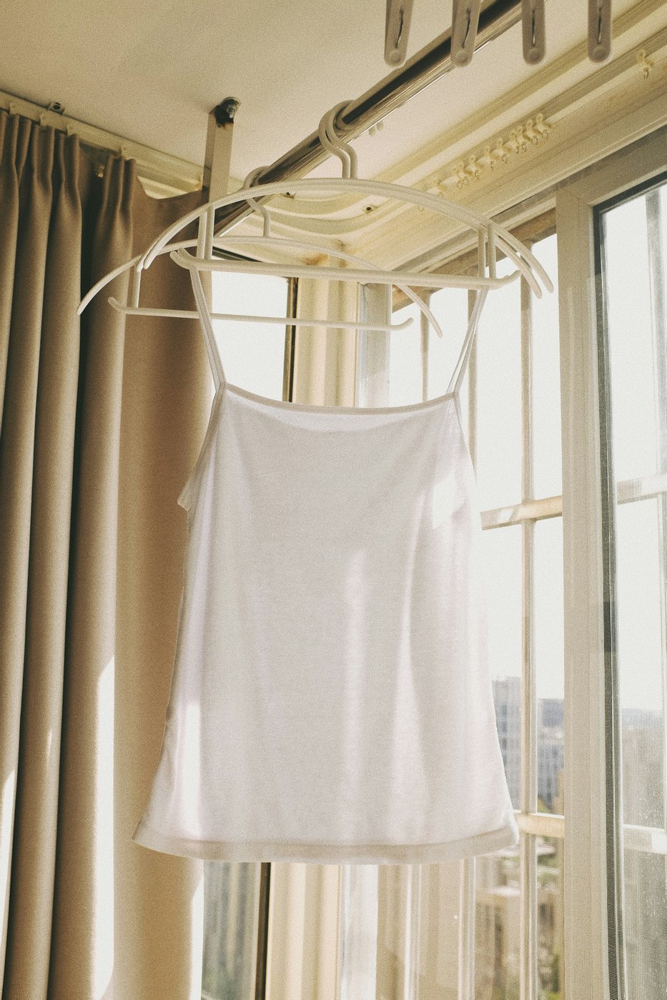 White cami top on a hanger by a sunlit window.