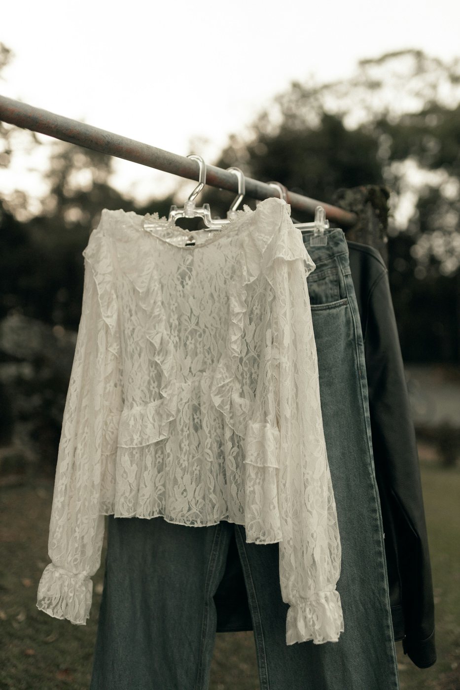 Ivory lace blouse with ruffles and long sleeves on a clothes rail outdoors.
