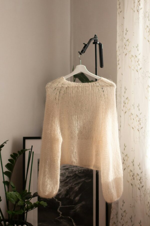Cream mohair sweater with balloon sleeves on a hanger in a bright room.